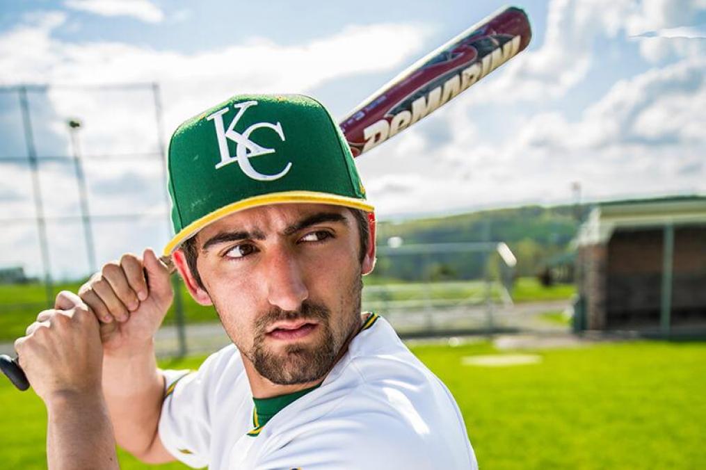 shoulders and above photo of a Keuka College athlete holding a baseball bat wearing a KC ball cap