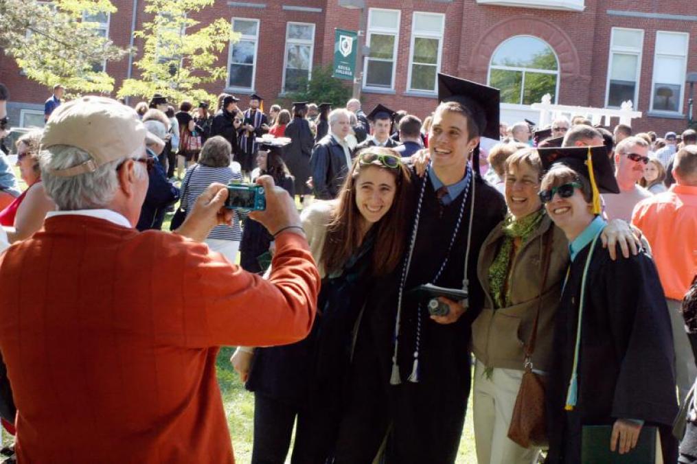 man taking a photo of two graduates in their cap and gown with two family members