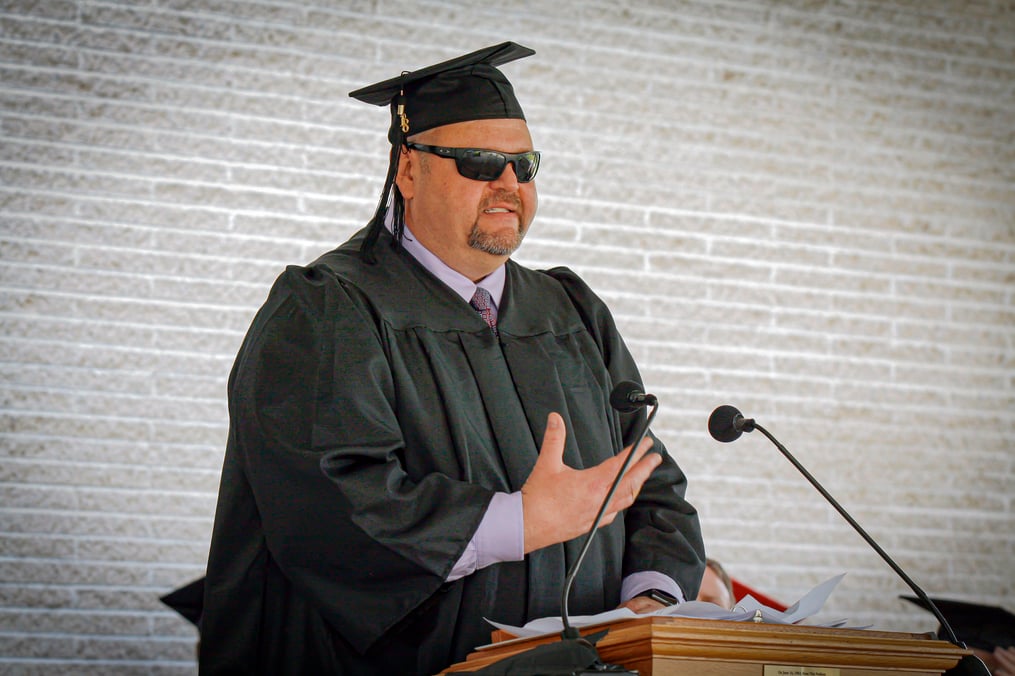 Guy in his cap and gown speaking at a podium at graduation