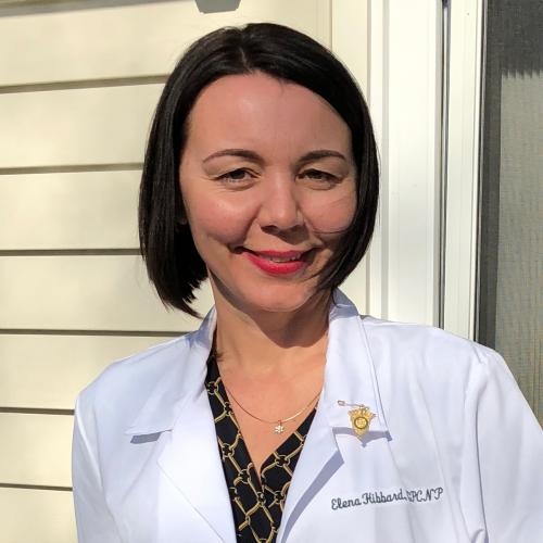 Elena Hibbard, an RN to BSN and NP graduate, outside her house wearing her lab coat.