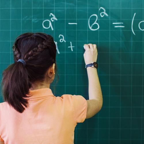 Young student standing in front of a chalk board writing math formulas on it